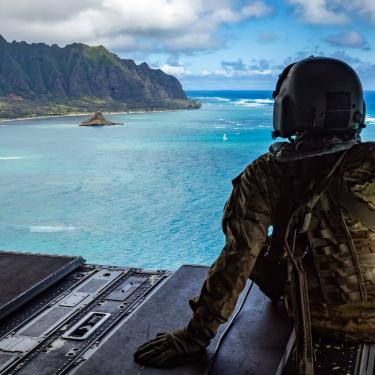 soldier in helicopter looking at pacific island mountians
