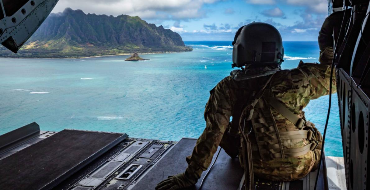 soldier in helicopter looking at pacific island mountians