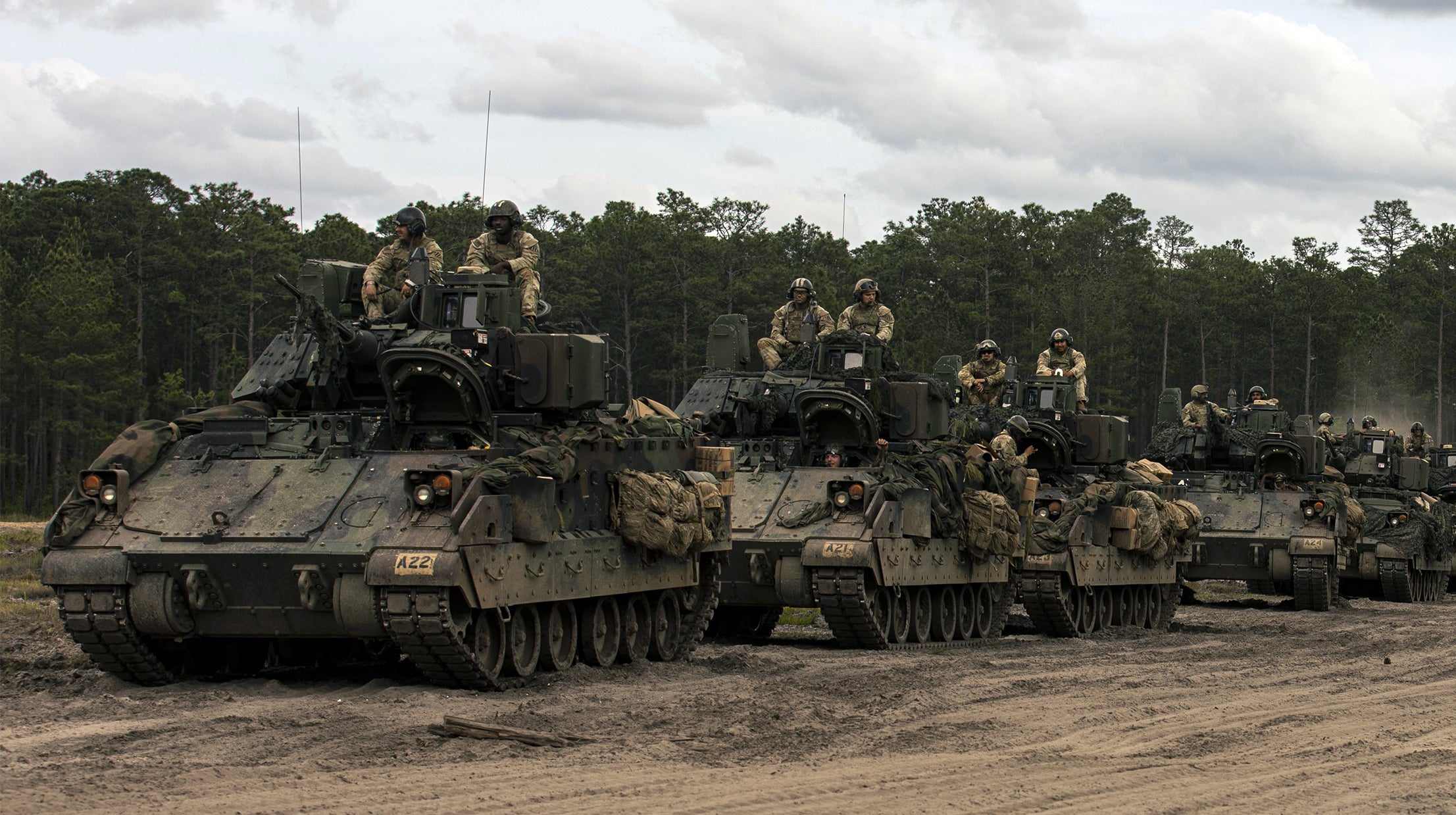 Four Bradley Fighting Vehicles in a line with Soldiers sitting atop