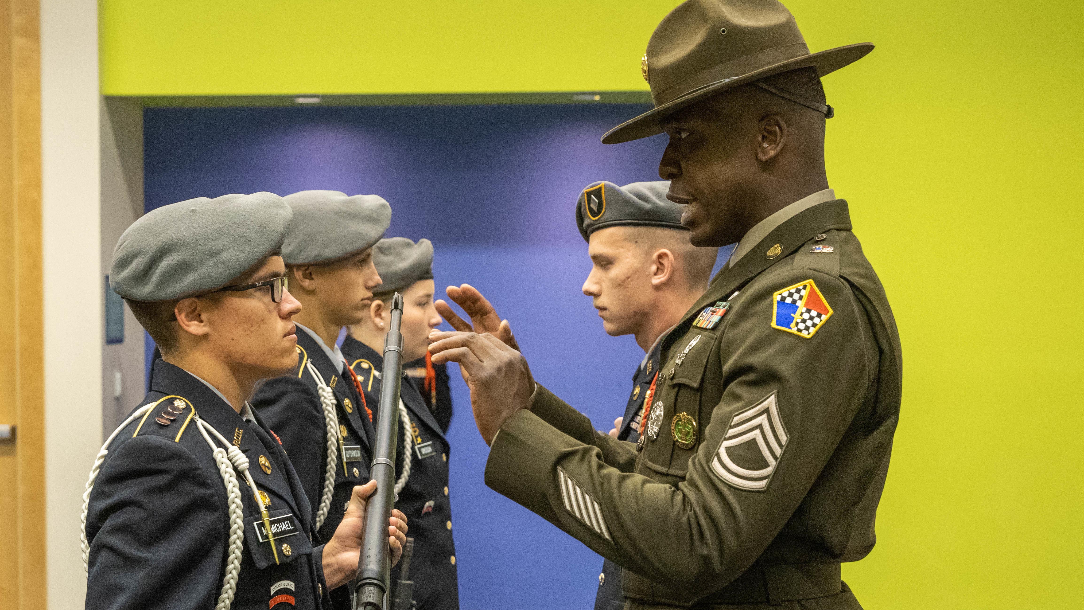 A drill sergeant inspects a junior ROTC member's rifle.