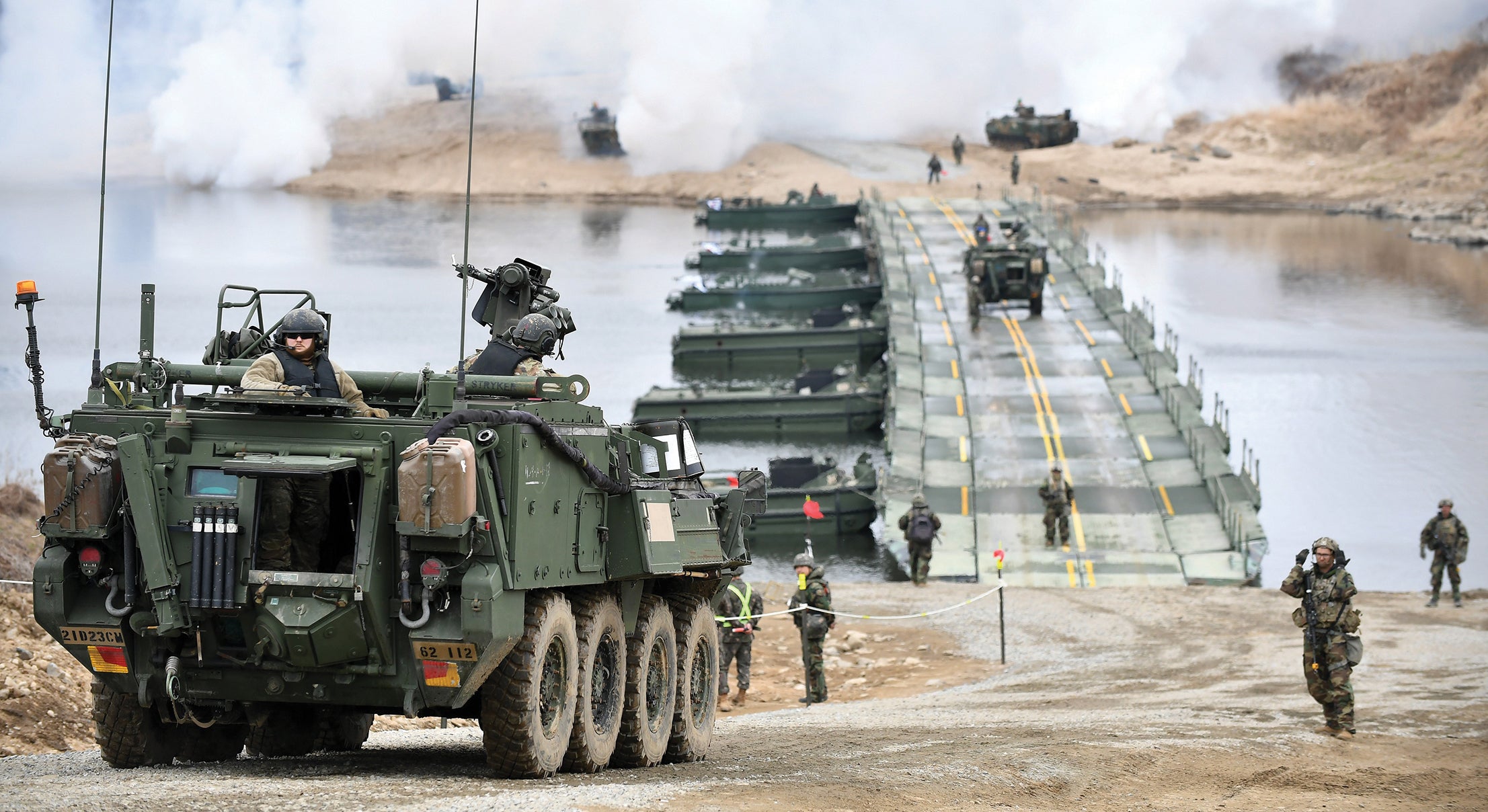 armored vehicles crossing a river over a temporary bridge