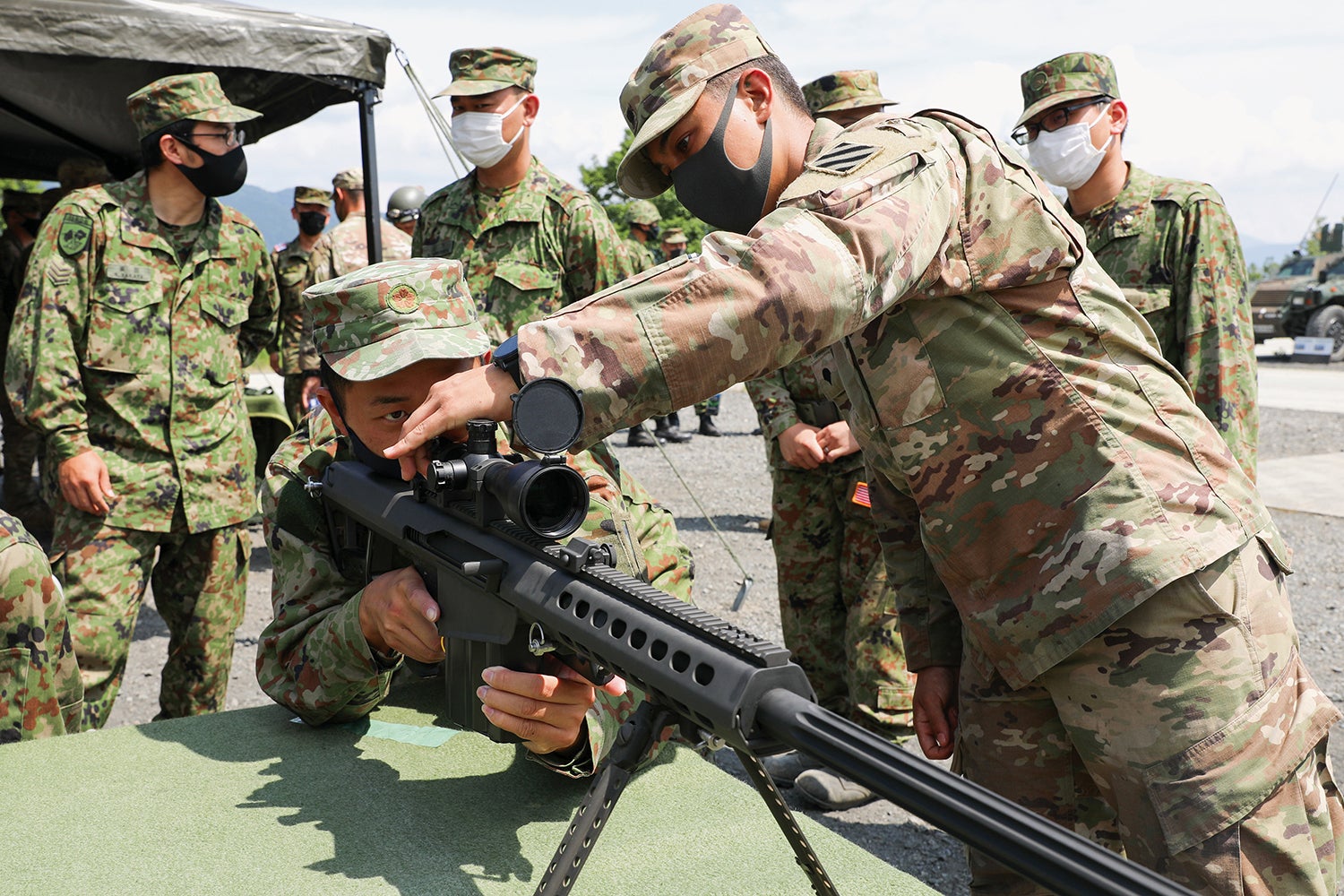 Spc. Gary Guijarro, with the 3rd Infantry Division, shows a Japan Ground Self-Defense Force member the optics on his rifle at Aibano Training Area, Japan. (Credit: U.S. Army/Pfc. Anthony Ford)